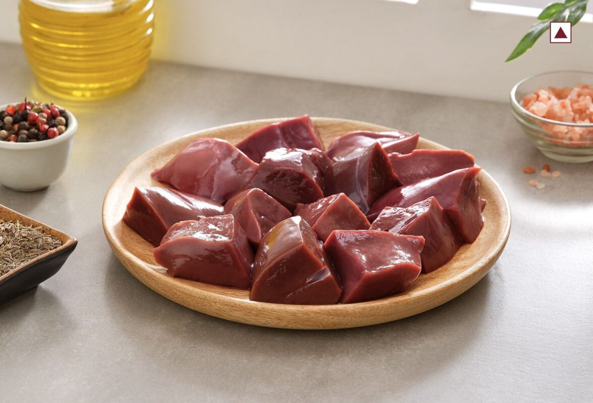 A wooden plate filled with cubed mutton liver sits on a kitchen counter, surrounded by bowls of spices, pink salt, and a bottle of oil, indicating preparation for cooking. Smart Chicken