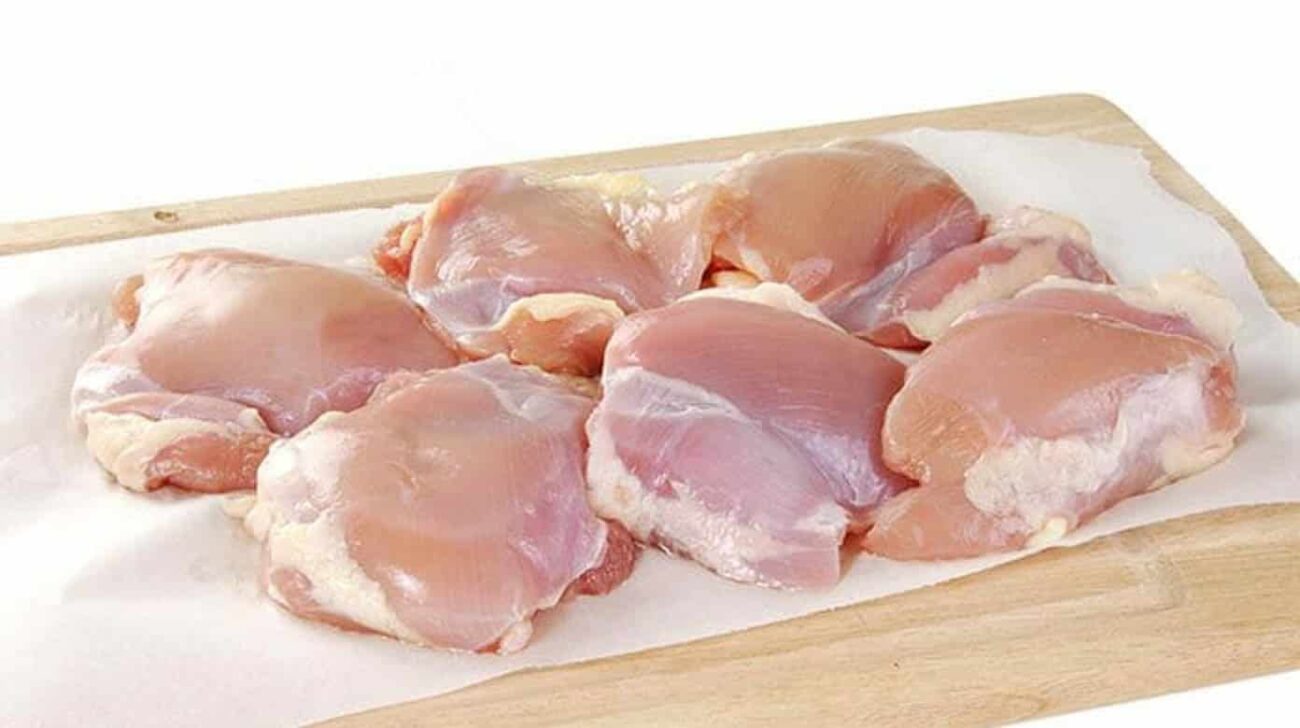 Boneless chicken thighs from a 1 kg pack are placed on a wooden cutting board lined with parchment paper, grouped together, and ready for preparation or cooking. Smart Chicken